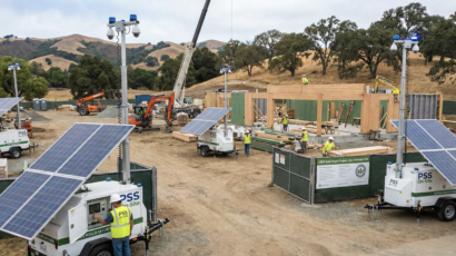 A large construction site with several Solar portable construction security units, workers, and building frameworks, set against a hilly landscape.